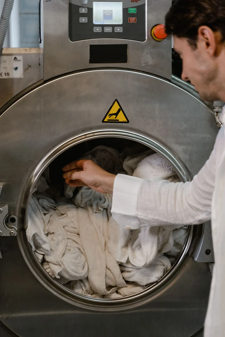 Man loading towels and white clothes into a large stainless steel industrial washing machine