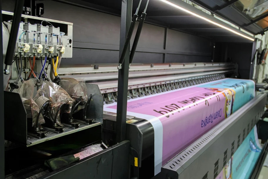 Wide-format printer feeding a long printed roll in pink and blue