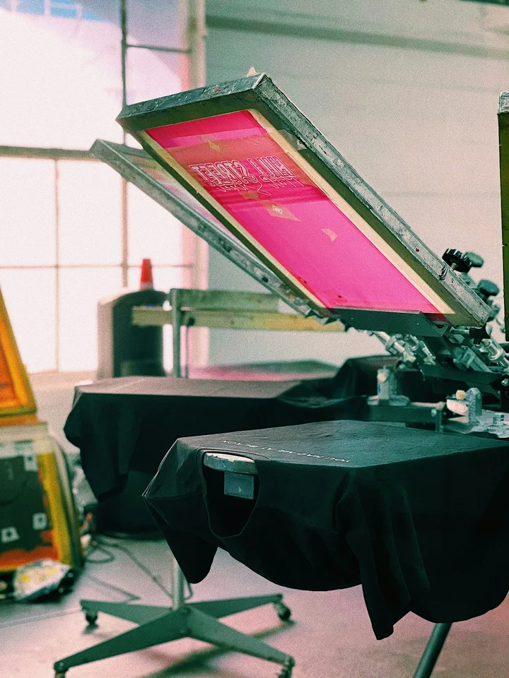 Makineri serigrafie me një ekran rozë të ngritur mbi një bluzë të zezë