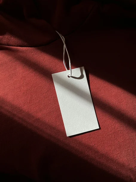 Blank white swing tag hanging on a string over red fabric