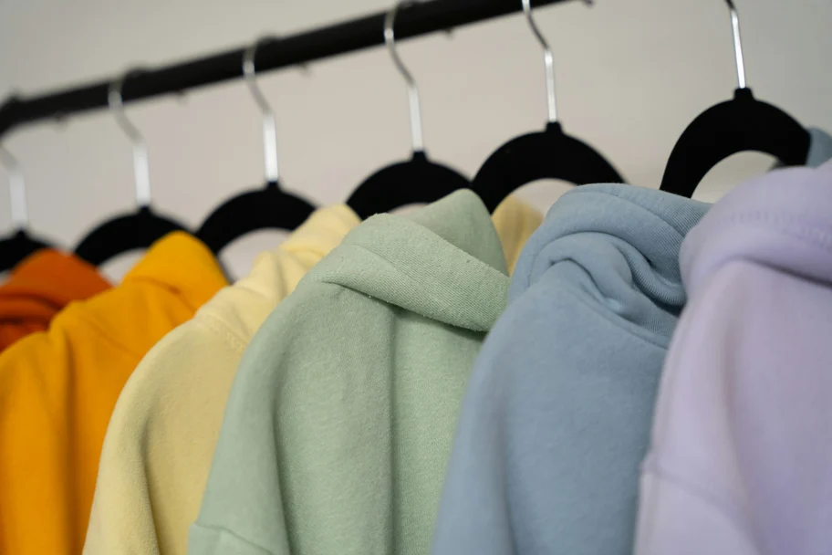 Kapuzenpullover in Orange, Gelb, Grün, Blau und Flieder hängen nebeneinander an einer Kleiderstange