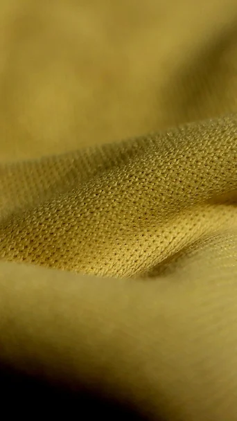Nahaufnahme eines gelben Strickstoffs mit feiner, waffelartiger Struktur, der in weichen Falten liegt